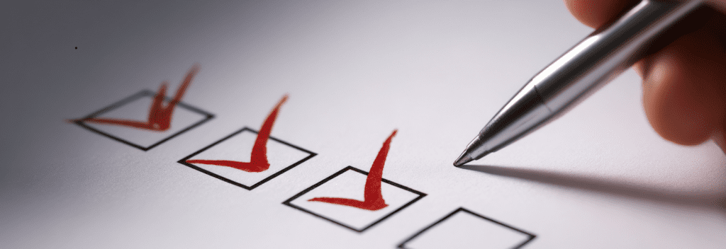 A close-up of a silver pen marking red checkmarks in a row of checkboxes on a white sheet of paper.