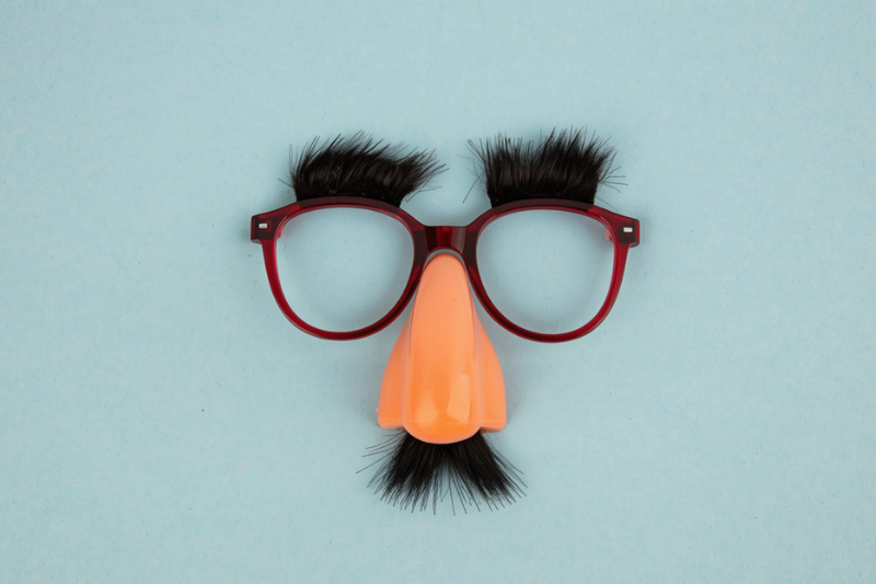 A pair of novelty glasses with fake black eyebrows, a large plastic nose, and a black mustache on a light blue background.