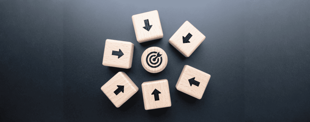 Seven wooden blocks with black arrows point towards a central round block featuring a target icon, all arranged on a dark background.