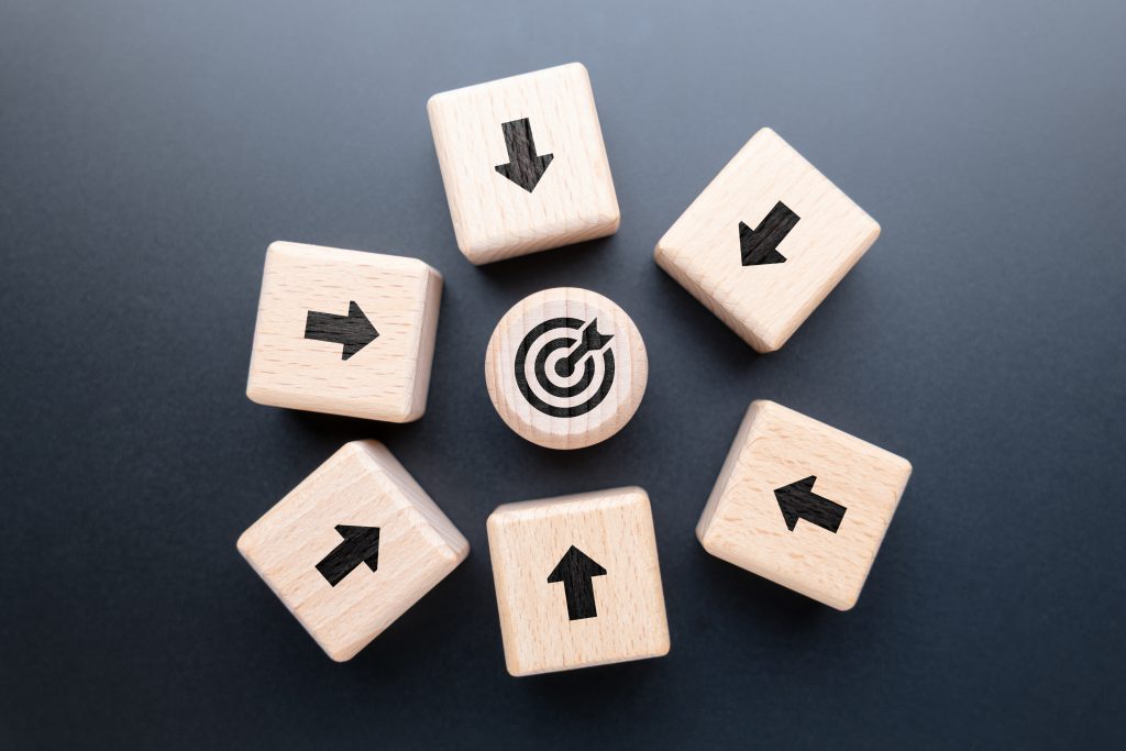 Six wooden blocks with black arrows point toward a central round block featuring a target symbol, all placed on a dark background.
